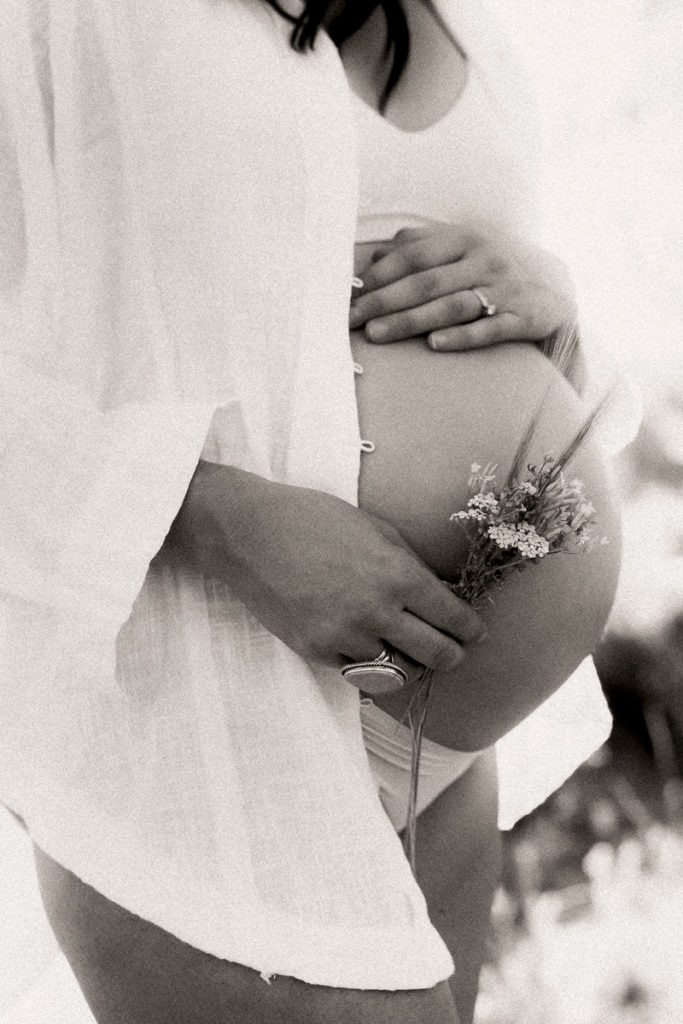 Maternity Photographer, a pregnant woman holds wildflowers near her exposed belly