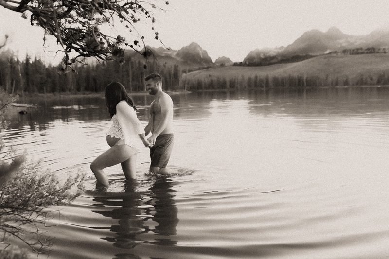 Maternity Photographer, pregnant woman holds hands with her husband as they walk out quiet waters