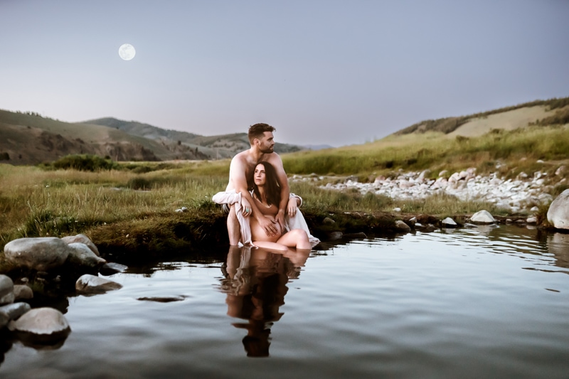 Maternity Photographer, a husband embraces his expecting wife as they sit in mountain streams